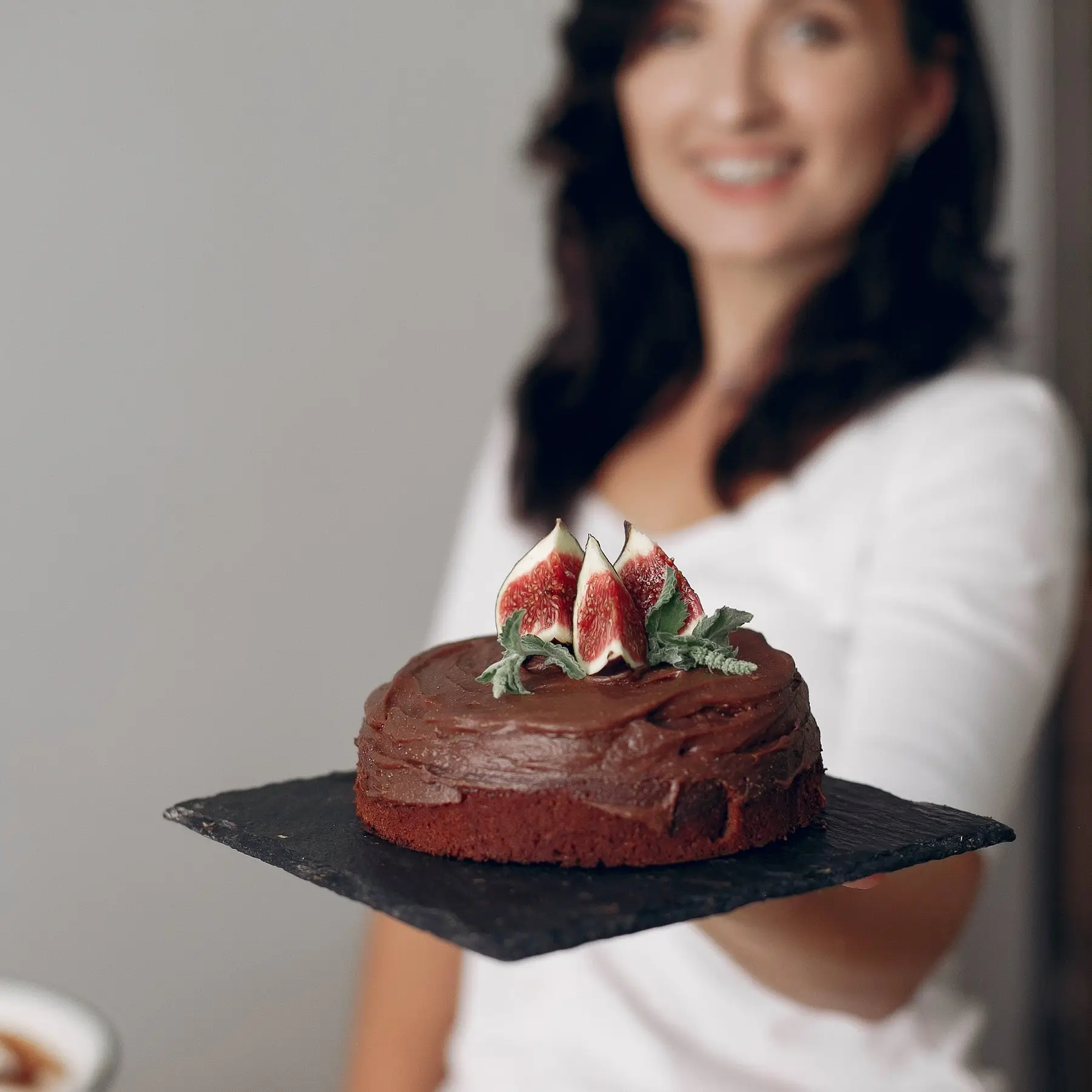 Anika Weiss presenting a chocolate cake topped with fresh figs in a bright studio setting.