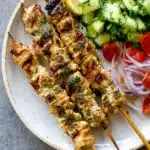 Easy Herby Lemon Skewers served with cucumber salad, tomatoes, onions, and lemon slices
