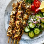 Lemon Skewers with grilled chicken served alongside cucumber salad and fresh lemon wedges