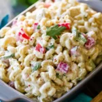 macaroni salad served in a dish with creamy dressing, red peppers, and fresh herbs