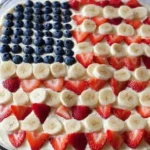 Patriotic Fruit Pizza decorated with strawberries, blueberries, and bananas in an American flag design