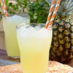 Pineapple Lemonade served over ice with fresh pineapple and striped paper straws