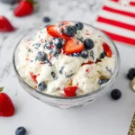 Red White and Blue Cheesecake Salad topped with strawberries, blueberries, and patriotic sprinkles in a glass bowl